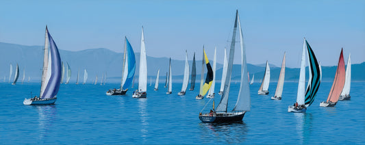 Sailing boats with colorful sails on a calm blue sea with mountains in the background